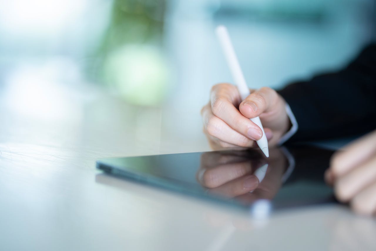 Close-up of a hand using a stylus on a tablet in a modern office, depicting digital work and productivity.